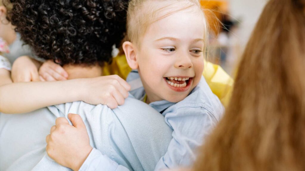 A child smiling warmly while hugging someone, showing autism and empathy through a joyful moment of connection