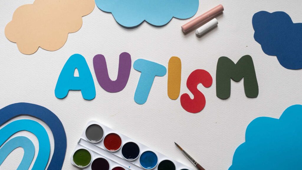 Art materials around the word “AUTISM,” creating a friendly visual that supports information about levels of autism.