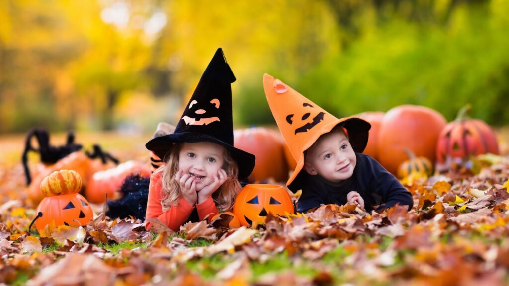 Two children wearing Halloween hats and playing outdoors with pumpkins
